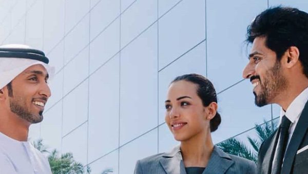 Two Middle Eastern businessman and business woman with traditional and suit clothes shaking hands on an agreement outside.